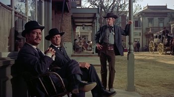 Movie still from “Gunfight at the O.K. Corral” (1957), directed by John Sturges – A group of men sitting next to each other on a sidewalk; Wide shot, Low angle