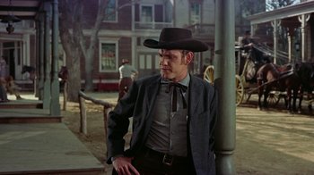 Movie still from “Gunfight at the O.K. Corral” (1957), directed by John Sturges – A man wearing a cowboy hat standing next to a pole; Medium shot, Low angle