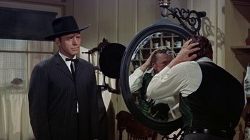 Movie still from “Gunfight at the O.K. Corral” (1957), directed by John Sturges – A man in a suit and hat looking in a mirror; Medium shot, Over the shoulder angle