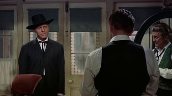 Movie still from “Gunfight at the O.K. Corral” (1957), directed by John Sturges – A man in a suit and a hat standing in front of another man in a suit and a hat; Medium shot, Over the shoulder angle