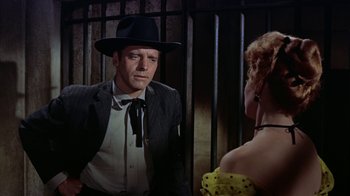 Movie still from “Gunfight at the O.K. Corral” (1957), directed by John Sturges – A man and a woman are standing next to each other in front of a fence; Medium shot, Low angle