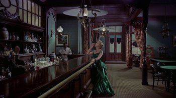 Movie still from “Gunfight at the O.K. Corral” (1957), directed by John Sturges – A woman in a green dress sitting at a bar; Wide shot, High angle