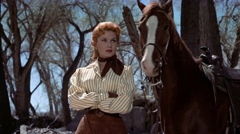 Movie still from “Gunfight at the O.K. Corral” (1957), directed by John Sturges – A woman standing next to a horse in a field; Medium shot, Low angle