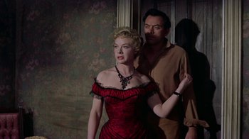 Movie still from “Gunfight at the O.K. Corral” (1957), directed by John Sturges – A woman in a red dress standing next to a man in a brown shirt; Medium shot, Low angle