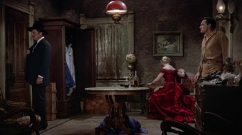Movie still from “Gunfight at the O.K. Corral” (1957), directed by John Sturges – A woman in a red dress sitting at a table in a room; Wide shot, High angle