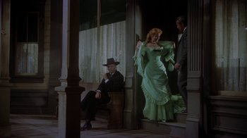 Movie still from “Gunfight at the O.K. Corral” (1957), directed by John Sturges – A man sitting on a chair next to a woman in a green dress; Wide shot, Low angle