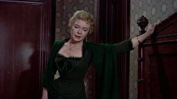 Movie still from “Gunfight at the O.K. Corral” (1957), directed by John Sturges – A woman in a green dress is standing in front of a wall; Medium shot, Low angle
