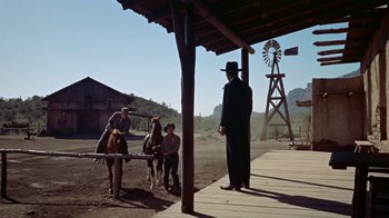 Movie still from “Gunfight at the O.K. Corral” (1957), directed by John Sturges – A group of people standing around a barn with horses; Wide shot, Over the shoulder angle