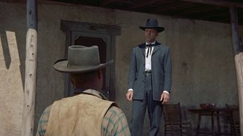 Movie still from “Gunfight at the O.K. Corral” (1957), directed by John Sturges – A man wearing a suit and hat standing next to a man wearing a hat; Medium shot, Over the shoulder angle