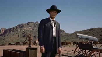 Movie still from “Gunfight at the O.K. Corral” (1957), directed by John Sturges – A man in a suit and hat standing in front of a herd of cattle; Medium shot, Low angle