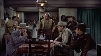 Movie still from “Gunfight at the O.K. Corral” (1957), directed by John Sturges – A group of people sitting around a table; Wide shot, High angle