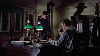Movie still from “Gunfight at the O.K. Corral” (1957), directed by John Sturges – A man in a top hat is writing at a desk; Wide shot, Low angle