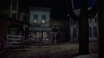 Movie still from “Gunfight at the O.K. Corral” (1957), directed by John Sturges – A man walking in the dirt next to a horse drawn carriage; Wide shot, Low angle
