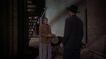 Movie still from “Gunfight at the O.K. Corral” (1957), directed by John Sturges – A man in a suit and a hat talking to another man in a suit; Medium shot, Over the shoulder angle