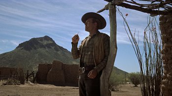 Movie still from “Gunfight at the O.K. Corral” (1957), directed by John Sturges – A man in a cowboy hat standing next to a wooden pole; Wide shot, Low angle