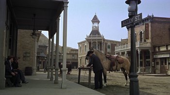 Movie still from “Gunfight at the O.K. Corral” (1957), directed by John Sturges – A man standing next to a horse on a dirt road; Wide shot, Low angle