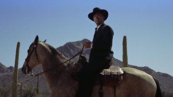 Movie still from “Gunfight at the O.K. Corral” (1957), directed by John Sturges – A man wearing a suit and hat riding a horse; Medium shot, Low angle