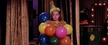 Movie still from “Gypsy” (1962), directed by Mervyn LeRoy – A young girl in a clown costume with balloons; Medium shot, High angle
