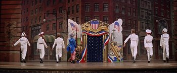 Movie still from “Gypsy” (1962), directed by Mervyn LeRoy – A stage set with flags and people in costumes; Wide shot, High angle