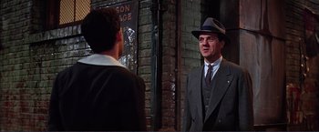 Movie still from “Gypsy” (1962), directed by Mervyn LeRoy – A man wearing a suit and hat talking to another man in a suit; Medium shot, Over the shoulder angle