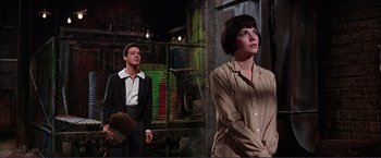 Movie still from “Gypsy” (1962), directed by Mervyn LeRoy – A man and a woman standing next to each other in front of a fence; Medium shot, Low angle