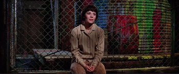 Movie still from “Gypsy” (1962), directed by Mervyn LeRoy – A woman sitting on the ground in front of a chain link fence; Medium shot, Low angle