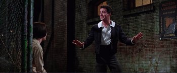 Movie still from “Gypsy” (1962), directed by Mervyn LeRoy – A man in a black suit and white shirt is smiling; Medium shot, Low angle