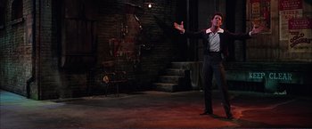 Movie still from “Gypsy” (1962), directed by Mervyn LeRoy – A man standing on a stage in front of a brick wall; Wide shot, Low angle