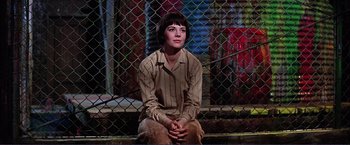 Movie still from “Gypsy” (1962), directed by Mervyn LeRoy – A woman sitting on the ground in front of a chain link fence; Medium shot, Low angle