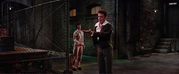 Movie still from “Gypsy” (1962), directed by Mervyn LeRoy – A man and a woman standing next to each other in front of a chain link fence; Medium shot, Low angle