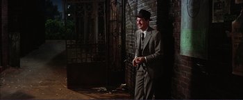 Movie still from “Gypsy” (1962), directed by Mervyn LeRoy – A man in a suit and hat standing in front of a brick wall; Medium shot, Over the shoulder angle