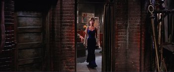 Movie still from “Gypsy” (1962), directed by Mervyn LeRoy – A woman in a blue dress standing in front of a brick wall; Wide shot, High angle