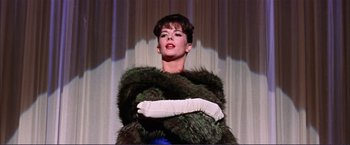 Movie still from “Gypsy” (1962), directed by Mervyn LeRoy – A woman in a green fur coat with a white arm cast; Medium shot, Low angle