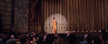 Movie still from “Gypsy” (1962), directed by Mervyn LeRoy – A woman in an orange outfit on a stage; Wide shot, Low angle