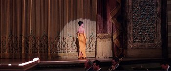 Movie still from “Gypsy” (1962), directed by Mervyn LeRoy – A woman in an orange dress standing on a stage; Wide shot, Low angle