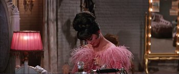 Movie still from “Gypsy” (1962), directed by Mervyn LeRoy – A woman in a pink dress and a pink feather boa; Medium shot, Low angle