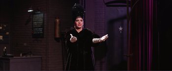 Movie still from “Gypsy” (1962), directed by Mervyn LeRoy – A woman dressed in a black outfit and wearing white gloves; Medium shot, Low angle