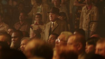 Movie still from “Hands of Stone” (2016), directed by Jonathan Jakubowicz – An older man in a brown suit and a brown hat is in a crowd; Medium shot, Over the shoulder angle