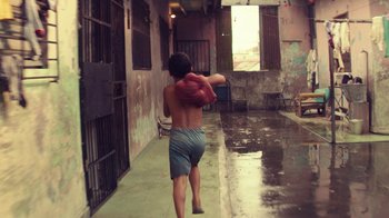 Movie still from “Hands of Stone” (2016), directed by Jonathan Jakubowicz – A young man walking down a street holding onto a bag; Wide shot, High angle
