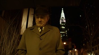 Movie still from “Hands of Stone” (2016), directed by Jonathan Jakubowicz – An older man in a hat and a coat stands in front of the empire state building at night; Medium shot, Low angle
