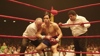 Movie still from “Hands of Stone” (2016), directed by Jonathan Jakubowicz – A man in a boxing ring being held by two men; Medium shot, Low angle