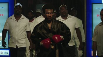 Movie still from “Hands of Stone” (2016), directed by Jonathan Jakubowicz – A group of men standing around a man wearing boxing gloves; Medium shot, Low angle