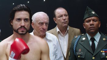 Movie still from “Hands of Stone” (2016), directed by Jonathan Jakubowicz – A group of men standing next to each other in a room; Medium shot, Over the shoulder angle