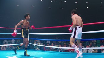 Movie still from “Hands of Stone” (2016), directed by Jonathan Jakubowicz – Two men in a boxing ring with spectators in the background; Wide shot, Over the shoulder angle