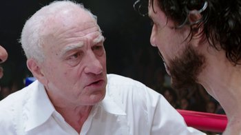 Movie still from “Hands of Stone” (2016), directed by Jonathan Jakubowicz – An older man talking to a younger man in front of an audience; Close Up shot, Over the shoulder angle