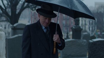 Movie still from “Hands of Stone” (2016), directed by Jonathan Jakubowicz – An older man in a suit and hat holding an umbrella; Medium shot, Over the shoulder angle