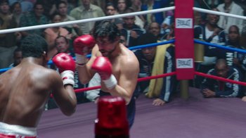 Movie still from “Hands of Stone” (2016), directed by Jonathan Jakubowicz – A man in a boxing ring hitting a punching bag; Close Up shot, Over the shoulder angle