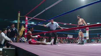 Movie still from “Hands of Stone” (2016), directed by Jonathan Jakubowicz – A man sitting on the ground in the middle of a boxing ring; Wide shot, High angle