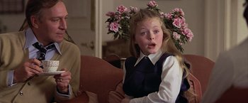 Movie still from “Hanover Street” (1979), directed by Peter Hyams – A young girl sitting in a chair in front of flowers; Medium shot, Over the shoulder angle