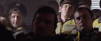 Movie still from “Hanover Street” (1979), directed by Peter Hyams – A man in a yellow jacket and a brown hat is looking at another man in a yellow jacket and a brown hat; Close Up shot, Over the shoulder angle
